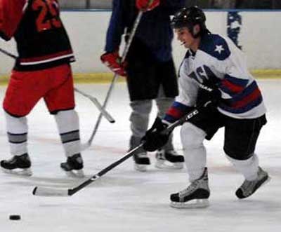 Zachary Cuddeback skating with the puck in a white USA jersey during a game